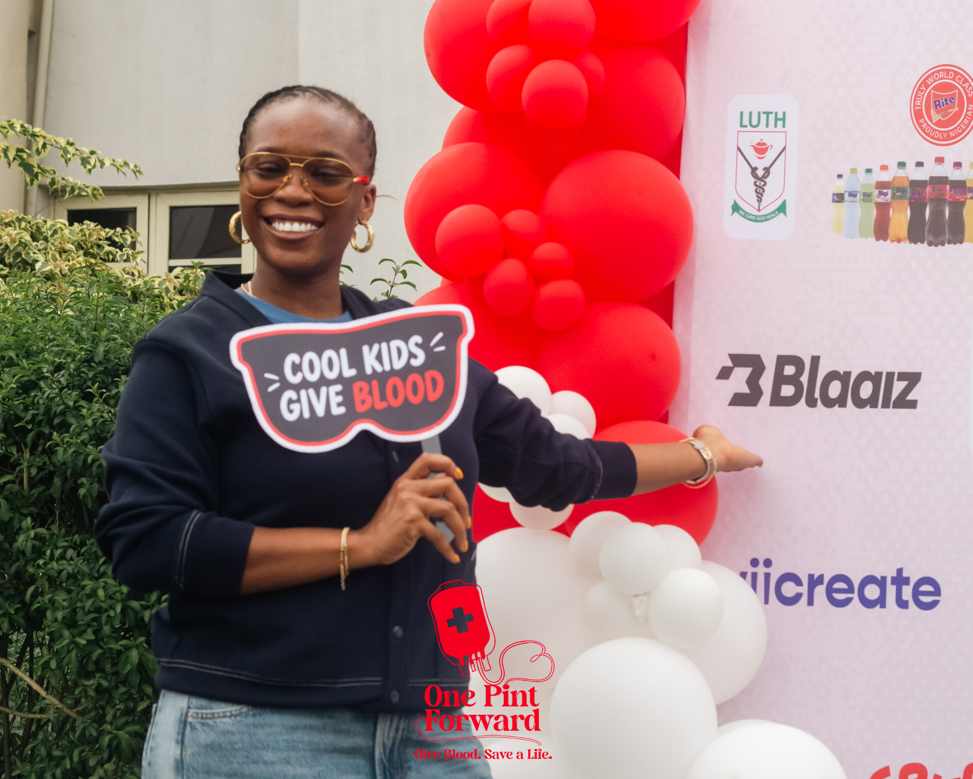 A supporter holding a Cool Kids Give Blood prop beside the red and white balloon arch