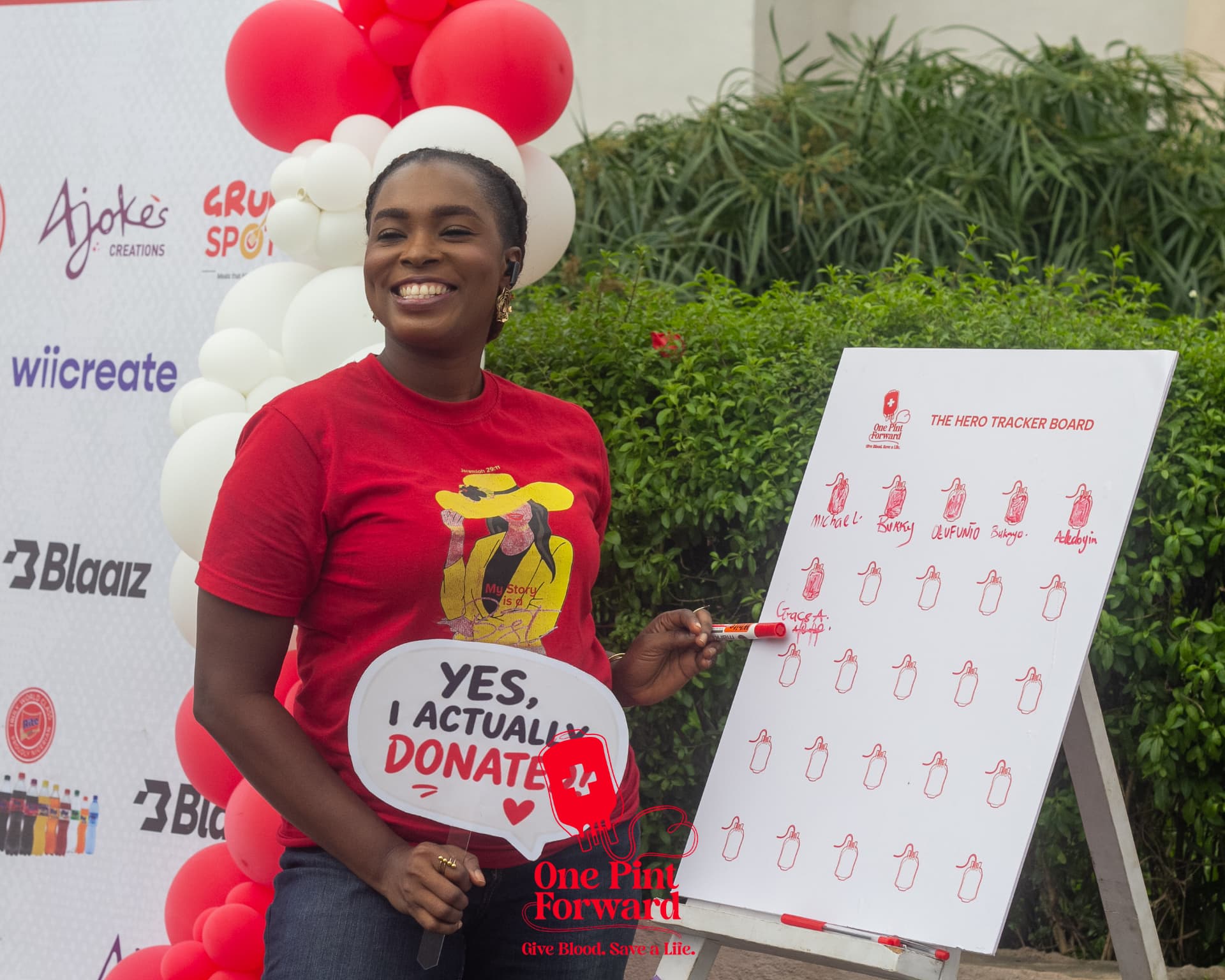 A smiling donor signing her name on the Hero Tracker Board while holding a Yes, I actually donate prop